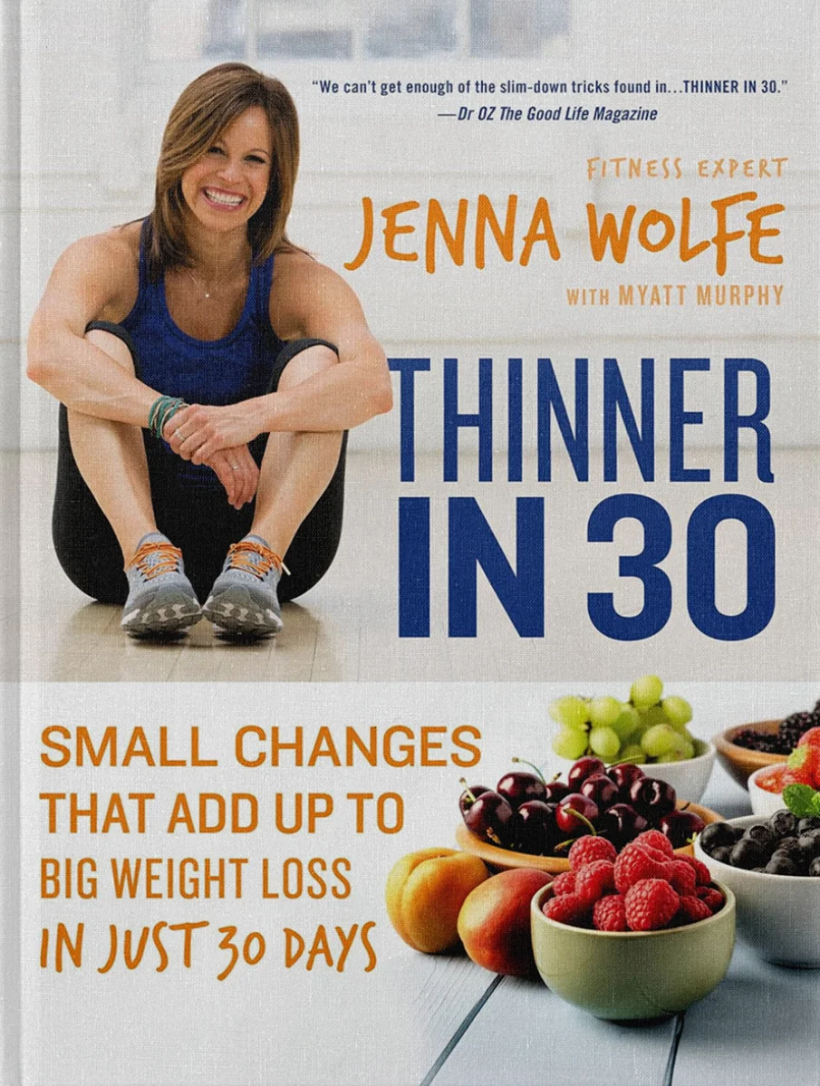 The cover of Jenna’s book titled “Thinner in 30” by Jenna Wolfe, with Myatt Murphy. The cover showcases Jenna Wolfe smiling and seated on the floor in a gym setting, wearing a blue tank top and sports leggings. She appears fit and happy, which aligns with the book’s theme of fitness and health. The cover also displays a variety of fresh fruits in bowls, emphasizing the book's focus on small changes leading to significant weight loss results in 30 days. Quotes and text on the cover highlight the endorsement by Dr. Oz and the practical approach of the book to achieving fitness and weight loss goals.